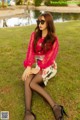 A woman sitting on the grass in a pink blouse and skirt.