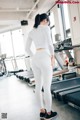 A woman in a white top and white leggings standing in a gym.