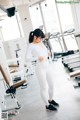 A woman in a white top and white leggings in a gym.