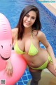 A woman in a yellow bikini sitting on an inflatable flamingo.