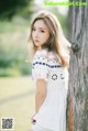 A woman leaning against a tree in a white dress.