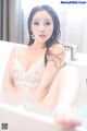 A woman in a white lingerie sitting in a bathtub.