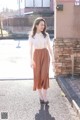 A woman in a white blouse and brown skirt is walking down the street.