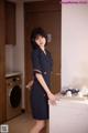 A woman in a blue dress standing next to a washing machine.