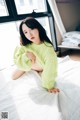 A woman in a green sweater sitting on a bed.