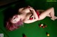 A woman laying on top of a pool table holding a red ball.