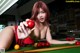 A woman in a red dress is playing pool.