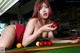 A woman laying on top of a pool table holding a red ball.