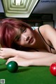 A woman laying on top of a pool table next to a green ball.