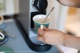 A person is pouring a cup of coffee into a coffee machine.