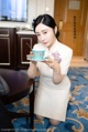 A woman in a white dress holding a cup and saucer.