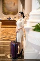 A woman in a white dress with a purple suitcase.