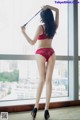 A woman in a red lingerie standing by a window.