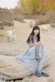 A woman sitting on a log in front of a herd of goats.