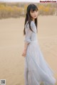 A woman in a long dress standing in the sand.