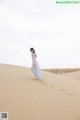 A woman in a blue dress walking on a sand dune.