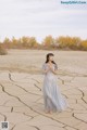 A woman in a long dress standing in the middle of a desert.