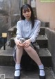 A woman sitting on the steps of a building wearing a school uniform.