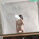 A naked woman taking a selfie in a bathroom mirror.