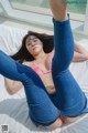 A woman in a pink bikini top and blue jeans laying on a bed.