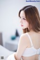 A woman in a white bra sitting on a bed.