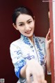 A woman in a blue and white cheongsam leaning against a wall.