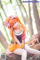 A woman with long orange hair sitting on a log in the woods.