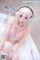 A woman with pink hair sitting in a bathtub with headphones on.