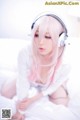 A woman with pink hair wearing headphones on a bed.