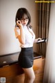 A woman in a white shirt and black skirt talking on a cell phone.