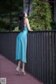 A woman in a blue dress leaning against a fence.