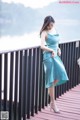 A woman in a blue dress standing on a wooden bridge.