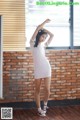 A woman in a white dress posing in front of a brick wall.