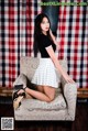 A woman sitting on a chair in front of a red and white checkered curtain.