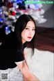 A woman sitting on the floor in front of a Christmas tree.