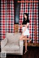 A woman sitting on a chair in front of a red and white checkered curtain.