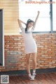 A woman in a white dress standing in front of a brick wall.