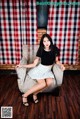 A woman sitting on a chair in front of a red and white checkered curtain.