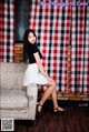 A woman sitting on a couch in front of a red and white checkered curtain.