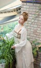 A woman in a white dress standing next to a plant.