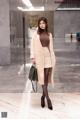 A woman in a beige coat is standing in a lobby.