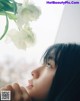 A woman looking out a window with a flower in her hand.