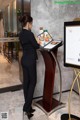 A woman standing in front of a menu on a stand.