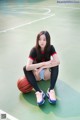 A woman sitting on a basketball court with a ball.