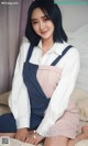 A woman sitting on top of a bed wearing a white shirt and blue overalls.