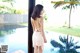 A woman in a white dress standing by a pool.