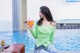 A woman sitting by a pool holding a glass of orange juice.