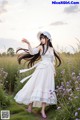 A woman in a white dress and hat standing in a field of flowers.