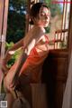 A woman in an orange dress leaning against a window.