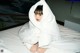 A woman sitting on a bed covered in a white blanket.